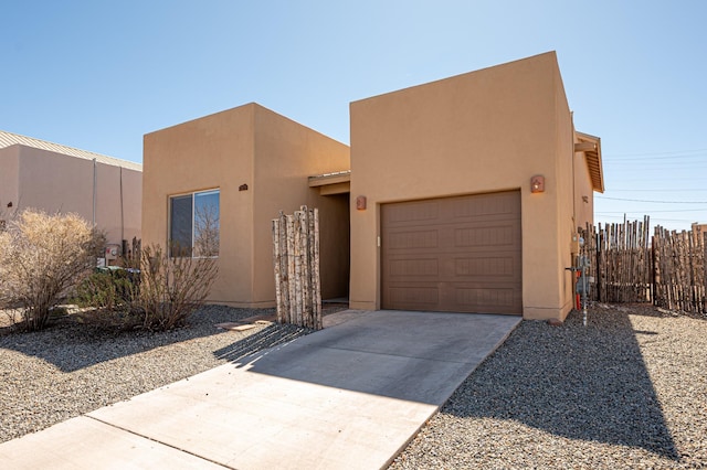pueblo revival-style home featuring concrete driveway, a garage, stucco siding, and fence