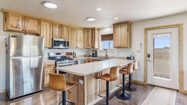 kitchen featuring a breakfast bar, a sink, stainless steel appliances, light countertops, and a textured ceiling