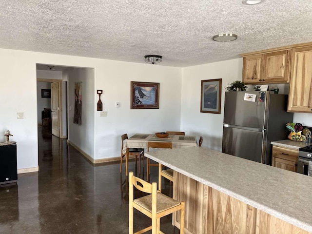 kitchen featuring a kitchen breakfast bar, a textured ceiling, freestanding refrigerator, concrete floors, and baseboards