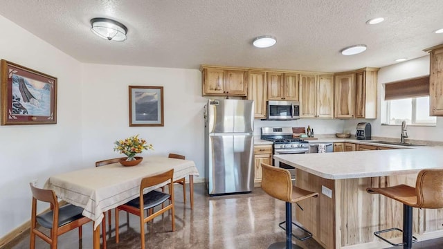 kitchen with a sink, finished concrete floors, appliances with stainless steel finishes, a breakfast bar area, and light countertops
