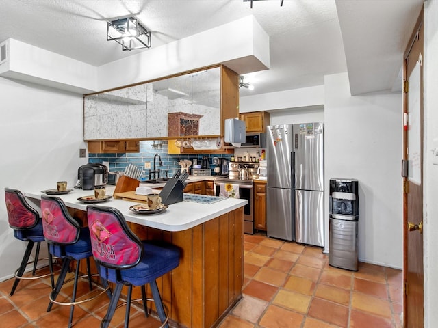 kitchen featuring backsplash, a breakfast bar area, appliances with stainless steel finishes, a peninsula, and brown cabinetry