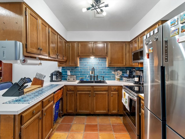 kitchen featuring a sink, backsplash, appliances with stainless steel finishes, brown cabinetry, and light countertops