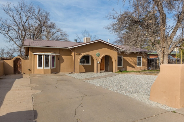 view of front of house featuring stucco siding, fence, driveway, and metal roof