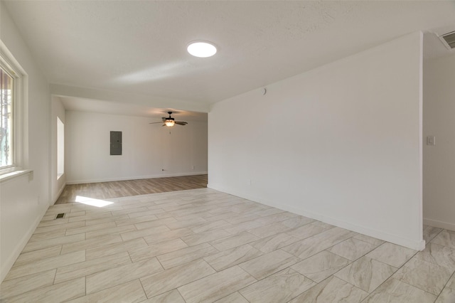 spare room featuring a ceiling fan, electric panel, and baseboards