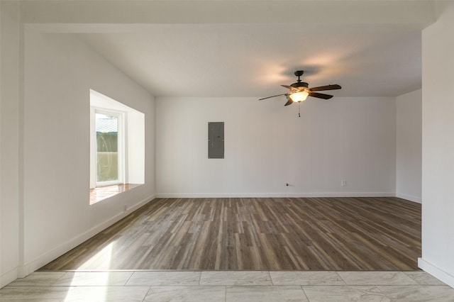 empty room featuring electric panel, ceiling fan, wood finished floors, and baseboards