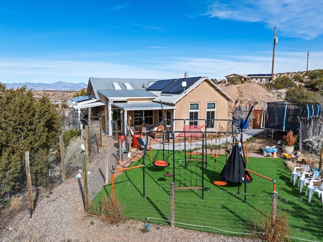 75A Camino Chupadero, Santa Fe, NM 87506 - back of house with stucco siding, fence, a trampoline, a yard, and roof mounted solar panels