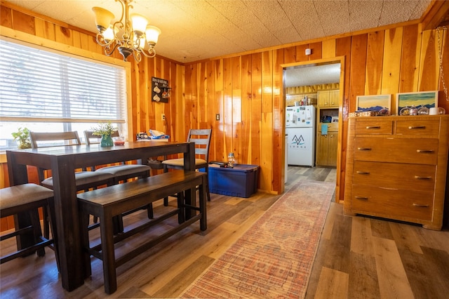dining space with wood walls, an inviting chandelier, and light wood-type flooring