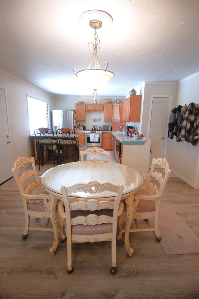 dining space with light wood-style flooring, ornamental molding, and baseboards