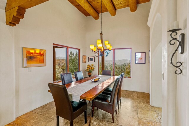 dining space featuring wooden ceiling, a chandelier, a towering ceiling, beam ceiling, and stone tile flooring