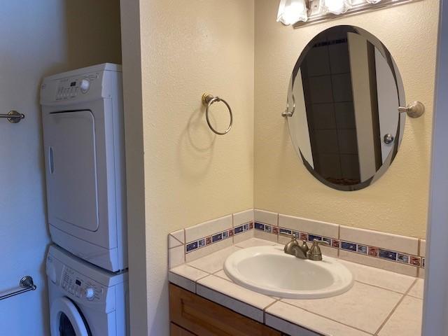 941 Calle Mejia Unit 207, Santa Fe, NM 87501 - bathroom with stacked washer / drying machine, vanity, and decorative backsplash