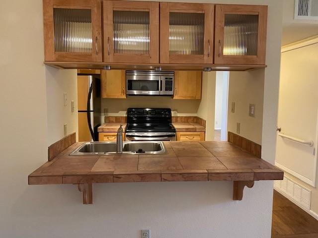 941 Calle Mejia Unit 207, Santa Fe, NM 87501 - kitchen with stainless steel appliances, a sink, a breakfast bar area, and glass insert cabinets