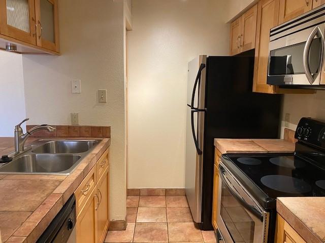 941 Calle Mejia Unit 207, Santa Fe, NM 87501 - kitchen featuring stainless steel appliances, a sink, baseboards, glass insert cabinets, and light tile patterned flooring