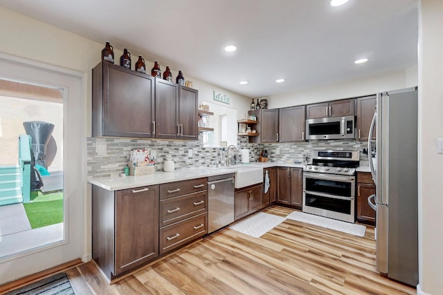 kitchen with light countertops, stainless steel appliances, a sink, open shelves, and light wood-style floors