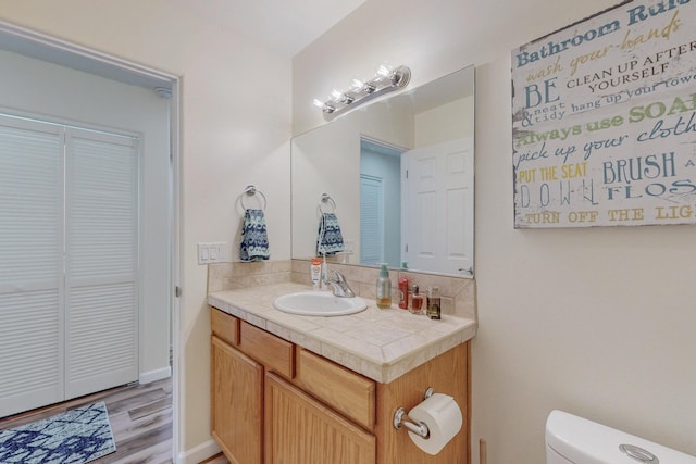 bathroom with vanity, toilet, baseboards, backsplash, and wood finished floors