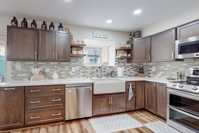 kitchen with light countertops, a sink, appliances with stainless steel finishes, and open shelves