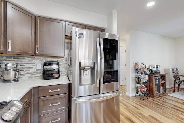 kitchen featuring light wood-style flooring, tasteful backsplash, stainless steel refrigerator with ice dispenser, light stone counters, and stove