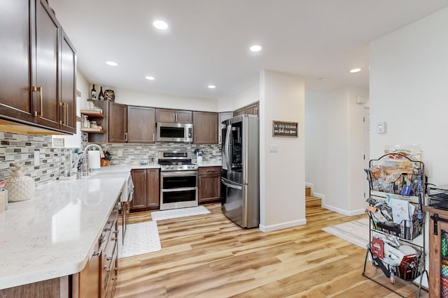 kitchen with light wood finished floors, a sink, stainless steel appliances, and open shelves