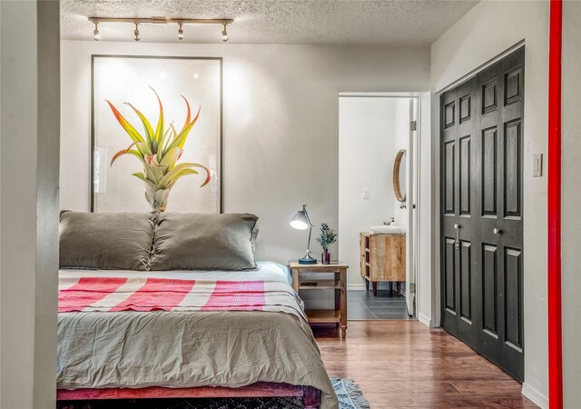 908 Rio Vista St, Santa Fe, NM 87501 - bedroom with wood finished floors, track lighting, ensuite bath, and a textured ceiling