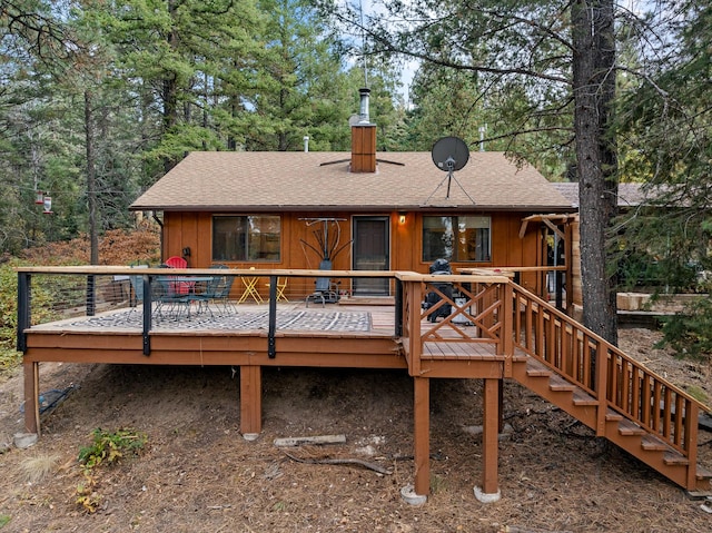rear view of house with a wooden deck, a chimney, and a shingled roof