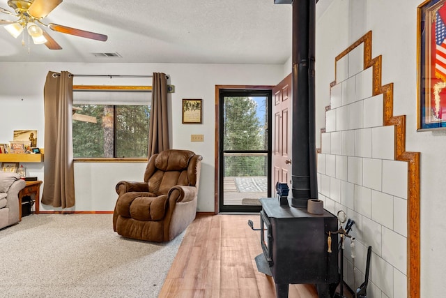 living area with a wood stove, ceiling fan, a textured ceiling, visible vents, and baseboards