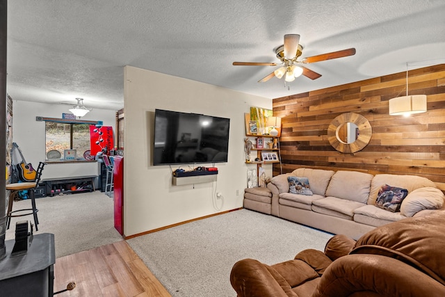 living room with baseboards, light wood-type flooring, a ceiling fan, a textured ceiling, and wooden walls