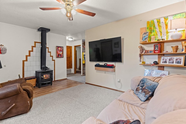 carpeted living area featuring visible vents, a wood stove, ceiling fan, and baseboards