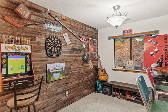 rec room featuring a textured ceiling, wooden walls, and carpet flooring