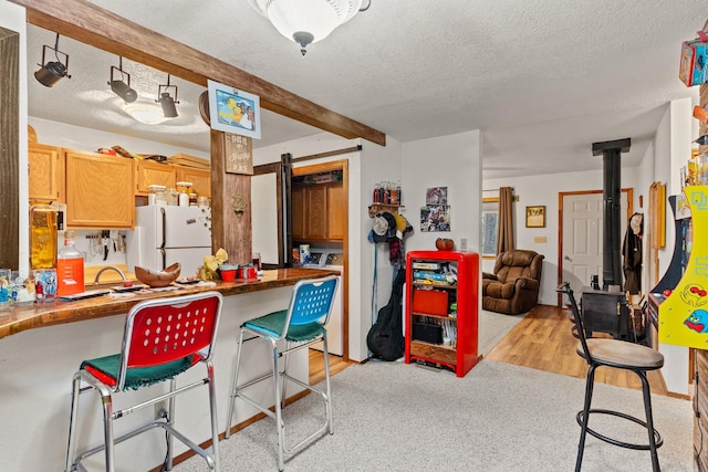 kitchen featuring open floor plan, a wood stove, freestanding refrigerator, a textured ceiling, and a breakfast bar area