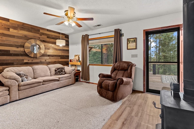 living area with wood walls, visible vents, a textured ceiling, and ceiling fan
