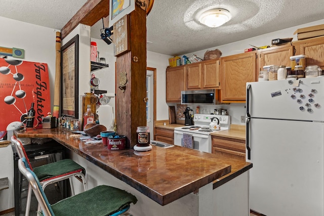 kitchen featuring a kitchen breakfast bar, white appliances, a peninsula, and a textured ceiling