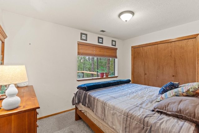 bedroom with a closet, baseboards, carpet flooring, a textured ceiling, and visible vents