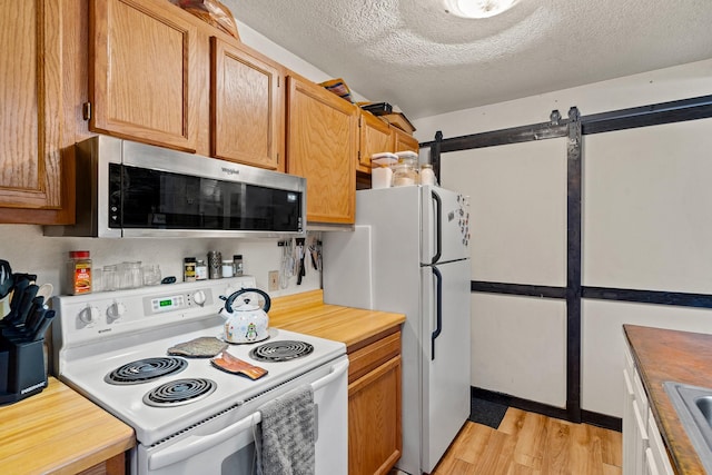 kitchen with white appliances, a textured ceiling, wooden counters, a barn door, and light wood finished floors