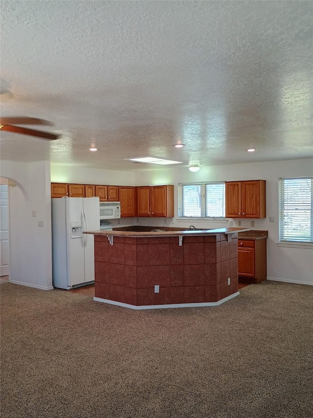 kitchen with brown cabinets, a ceiling fan, white appliances, and carpet