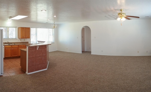 kitchen with ceiling fan with notable chandelier, a textured ceiling, arched walkways, light carpet, and a sink