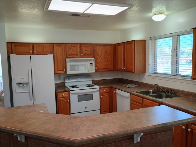 kitchen with visible vents, a sink, white appliances, a textured ceiling, and brown cabinetry