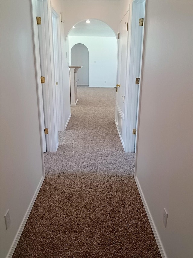 corridor featuring arched walkways, baseboards, and carpet floors