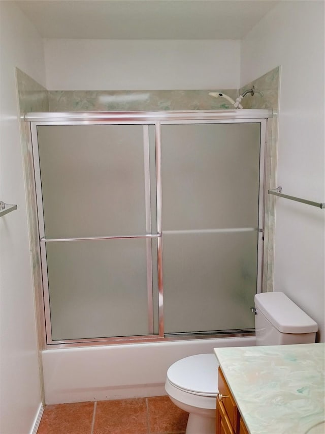 bathroom featuring toilet, combined bath / shower with glass door, vanity, and tile patterned flooring