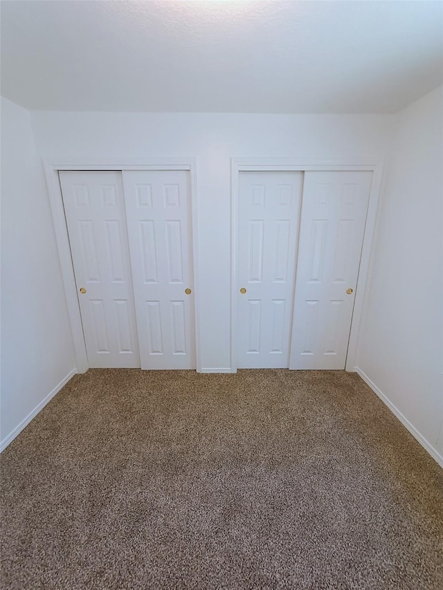 unfurnished bedroom with carpet, baseboards, and two closets