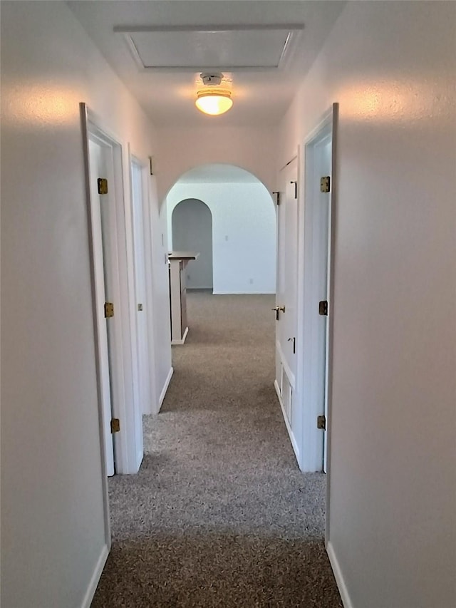 hallway featuring arched walkways, carpet flooring, and baseboards