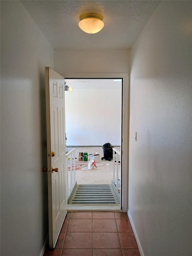 hallway featuring tile patterned floors, baseboards, and a textured ceiling