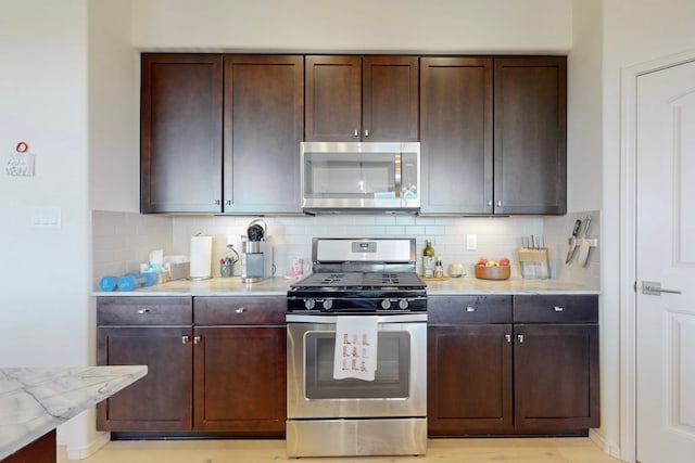 kitchen with stainless steel appliances, tasteful backsplash, dark brown cabinetry, and light stone counters