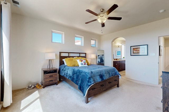 bedroom featuring baseboards, ensuite bathroom, ceiling fan, arched walkways, and light colored carpet