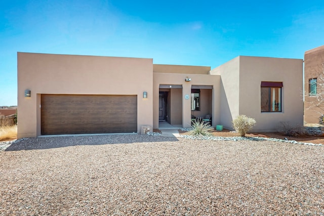 pueblo-style home with gravel driveway, stucco siding, and an attached garage