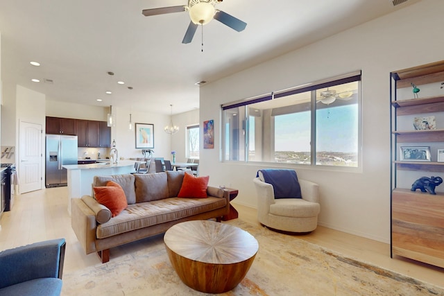living room with light wood-style flooring, recessed lighting, baseboards, and ceiling fan with notable chandelier