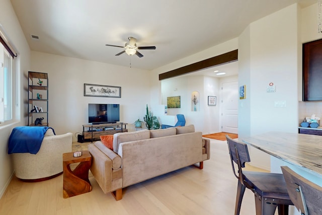 living area featuring visible vents, baseboards, light wood finished floors, and a ceiling fan
