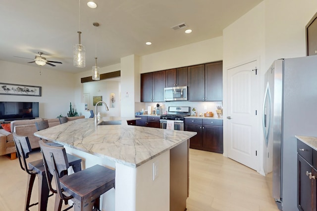 kitchen featuring a kitchen island with sink, visible vents, a breakfast bar area, stainless steel appliances, and a sink