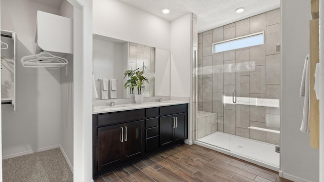 bathroom with wood finished floors, a sink, a stall shower, double vanity, and baseboards