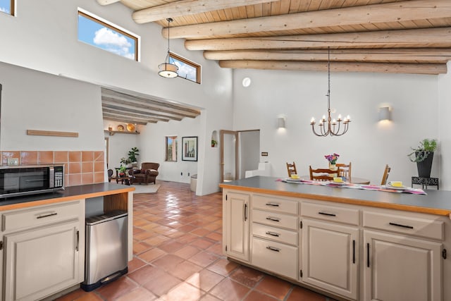 kitchen with a chandelier, wooden ceiling, stainless steel microwave, a high ceiling, and hanging light fixtures