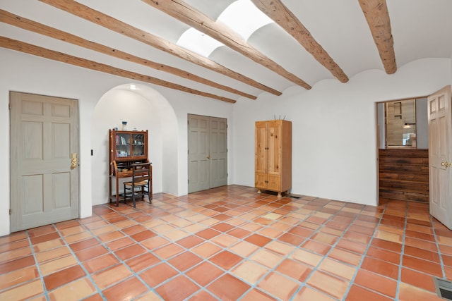 unfurnished room featuring arched walkways, light tile patterned floors, and beamed ceiling