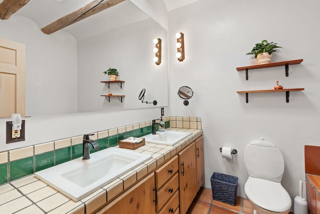 bathroom with double vanity, a sink, toilet, and beam ceiling